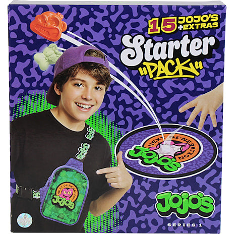 A boy wearing a purple FirstGrade bag smiles and points at the Jojo’s logo on a box. The packaging reads “First Grade: Jojo’s Starter Pack - Series 1” and displays colorful toy figures against a purple patterned background, hinting at exciting surprises such as rare JoJo cards from the premium booster set for collectors of FirstGrade’s JoJo’s Bizarre Adventure samlekort.